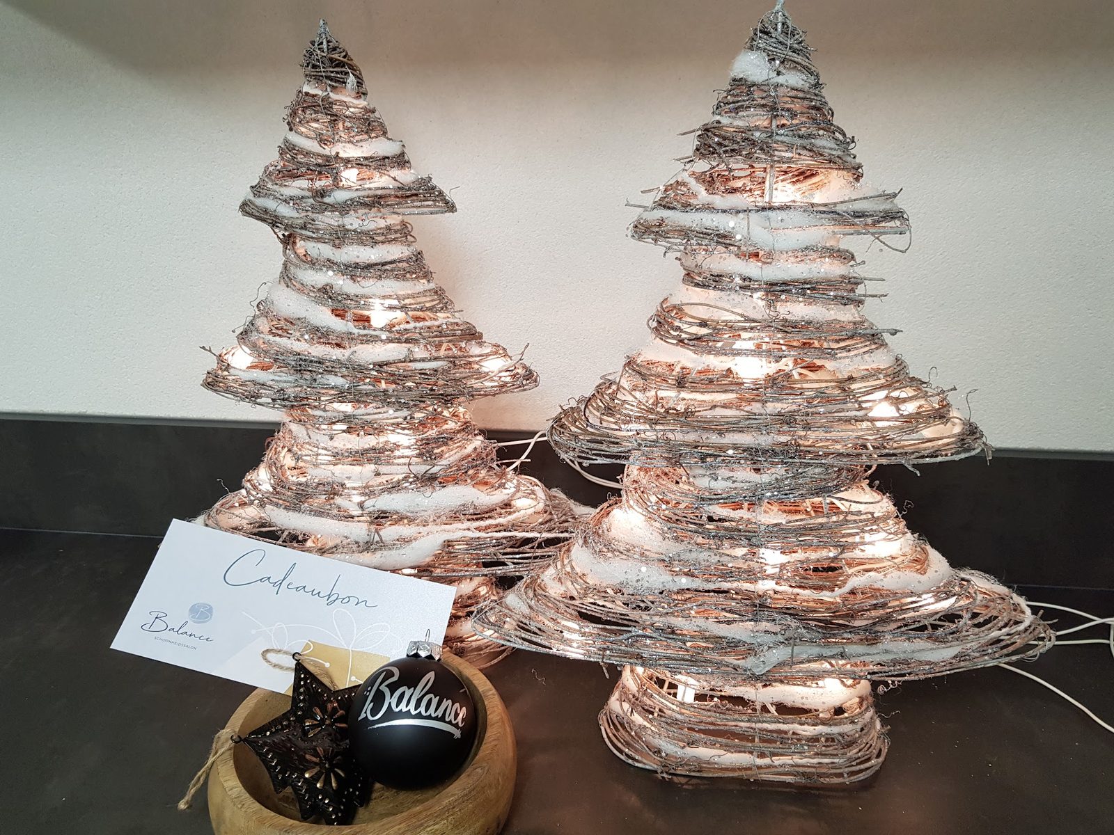 Lichtgevende kerstboompjes naast een cadeaubon van Balance