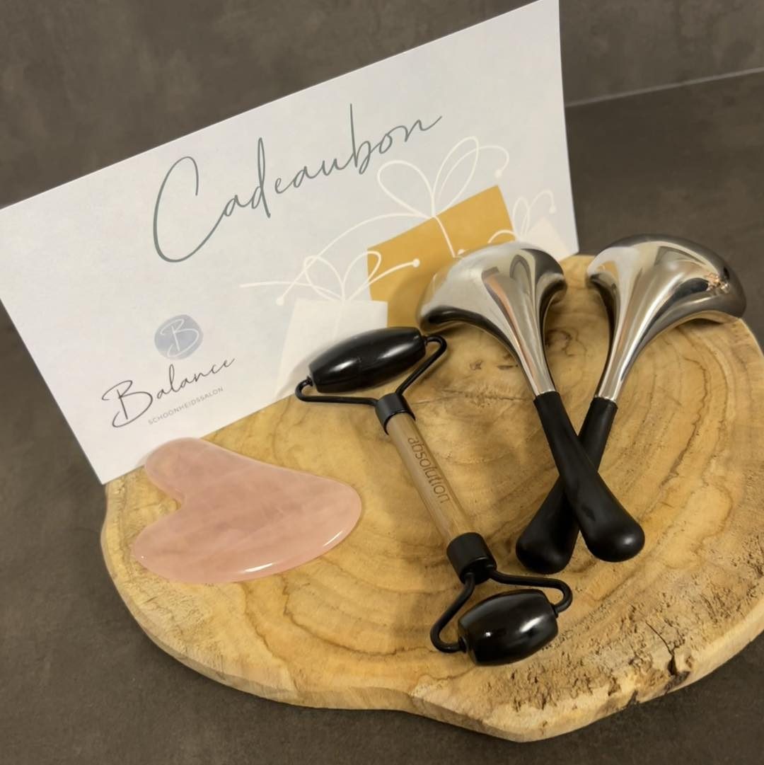 Een cadeaubon van Balance met een gua sha en gezichtsrollers op een houten schijf